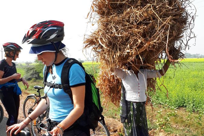 lady carrying straw bundle past cyclists
